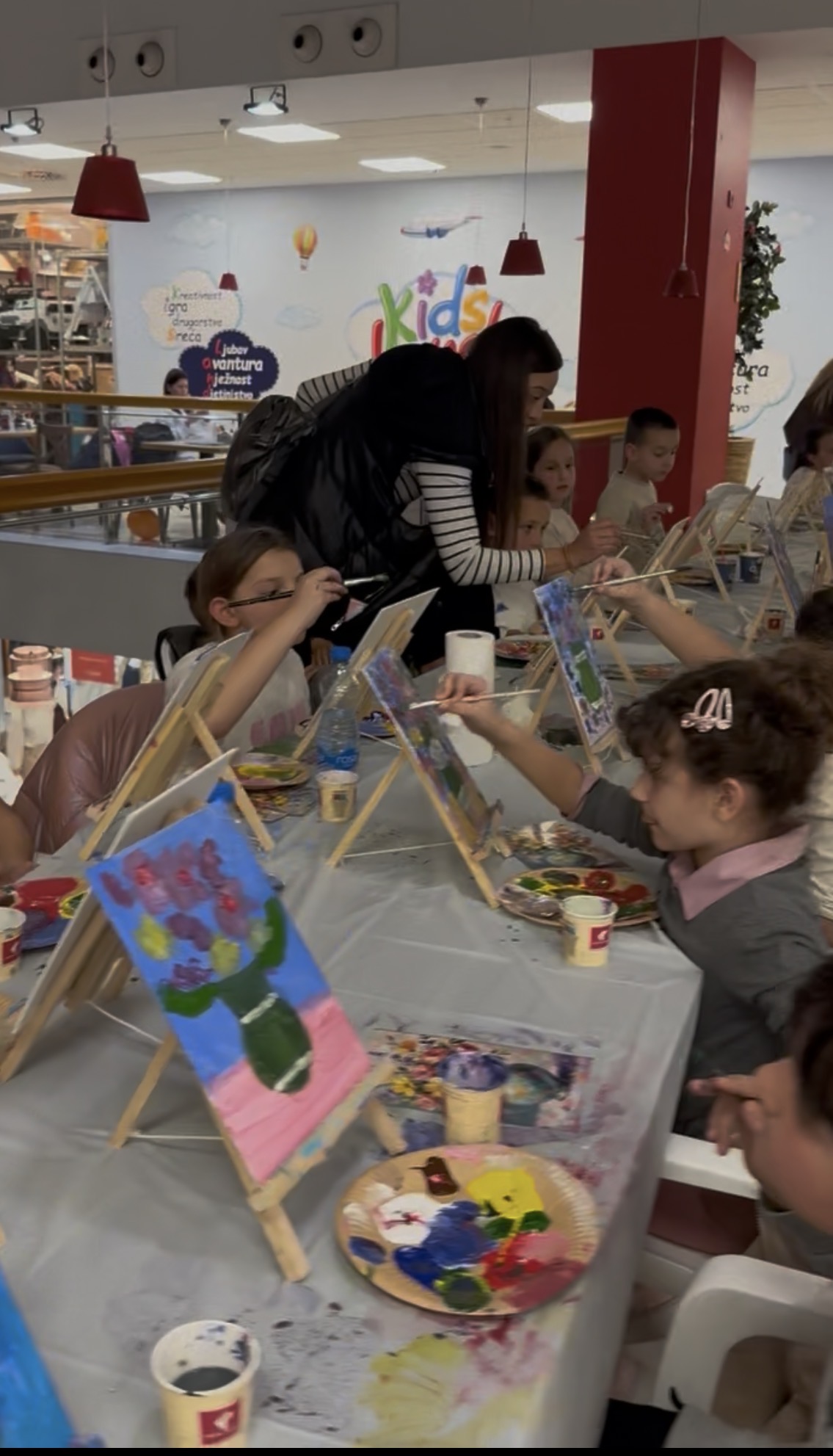 Children painting on canvas easels at a creative workshop in Shopping Centre Kamelija, Kotor